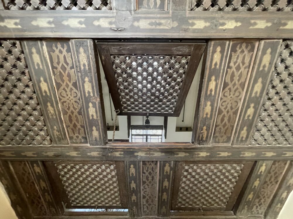Patterns and inlaid wooden frames surrounding a small window in the center that looks out to a large room.