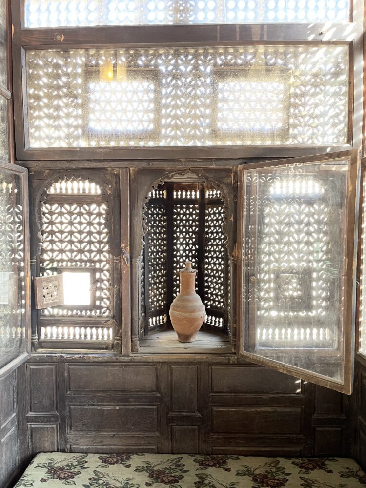 Patterned wood-turned lattice window screen; the center window panel is open and a ceramic jar rests in the open niche.